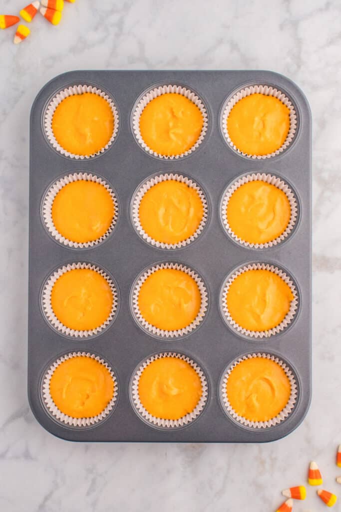 Cupcake liners now filled with orange batter on top of yellow layer before baking.