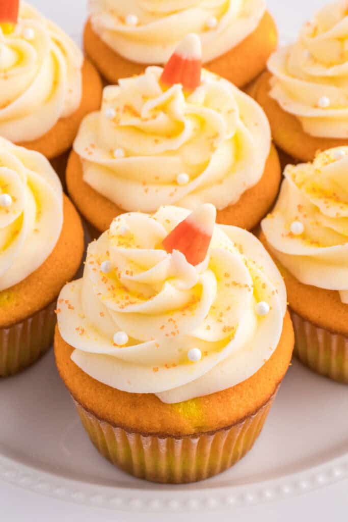 Close-up of frosted Candy Corn Cupcakes topped with white frosting swirls, candy corn, and sugar pearls.