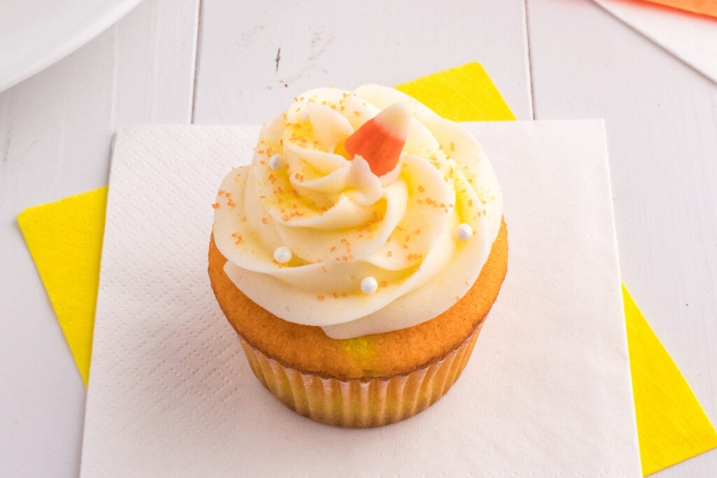 Single Candy Corn Cupcake on a napkin with yellow and white background showing detailed frosting and toppings.