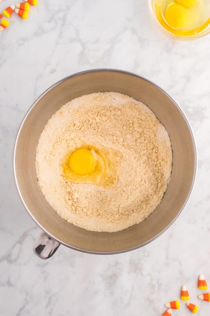 Mixing bowl showing coarse, crumbly batter with an egg cracked in the center ready to be mixed in.