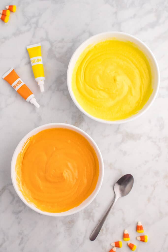 Two bowls of cupcake batter now fully colored - one bright yellow and one vivid orange - ready to be layered.