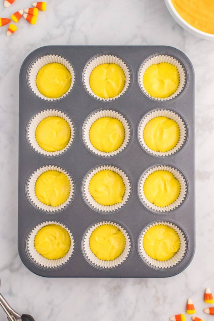 Cupcake liners partially filled with yellow batter as the first layer for Candy Corn Cupcakes.