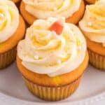 Square close-up of Candy Corn Cupcake topped with swirled white frosting, candy corn, and sugar pearls on a white plate.