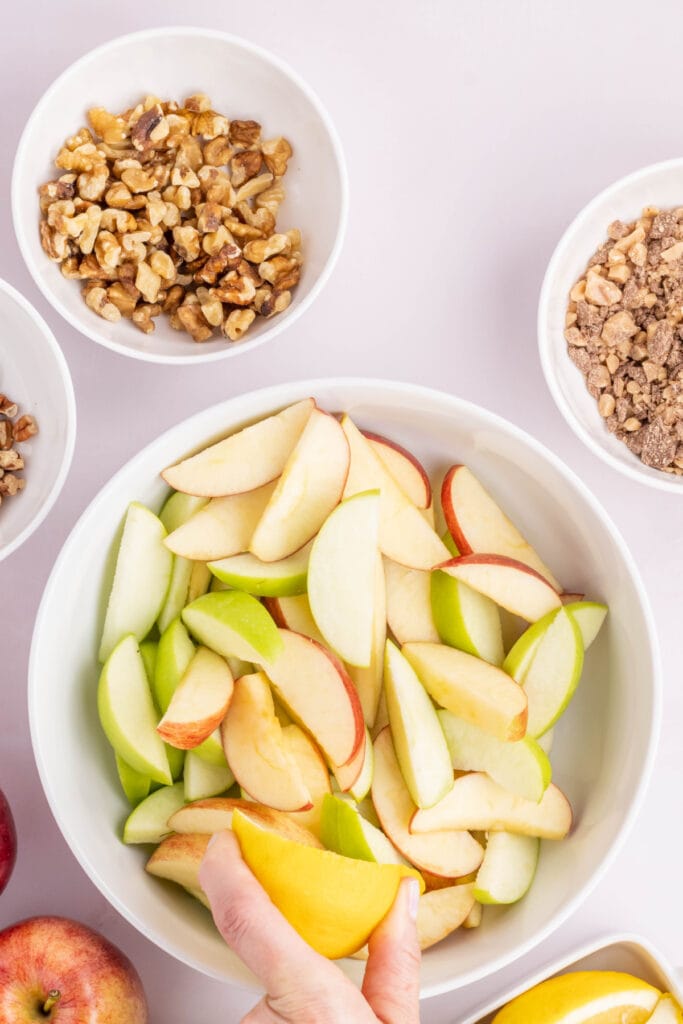 Bowl of red and green apple slices being coated with lemon juice to prevent browning.