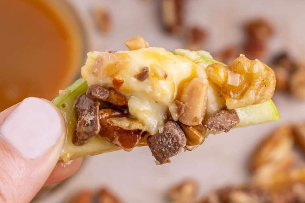 Close-up of caramel apple dip on an apple slice showing layers of caramel, nuts, and toffee.