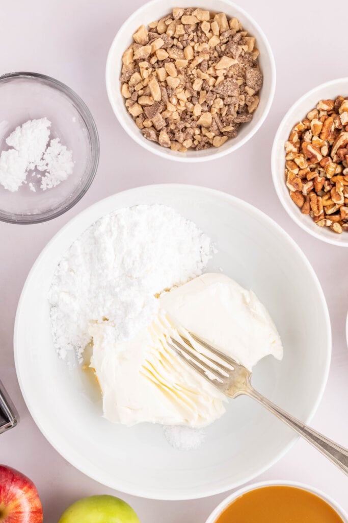 Fork beginning to blend cream cheese, powdered sugar, and vanilla in a mixing bowl.