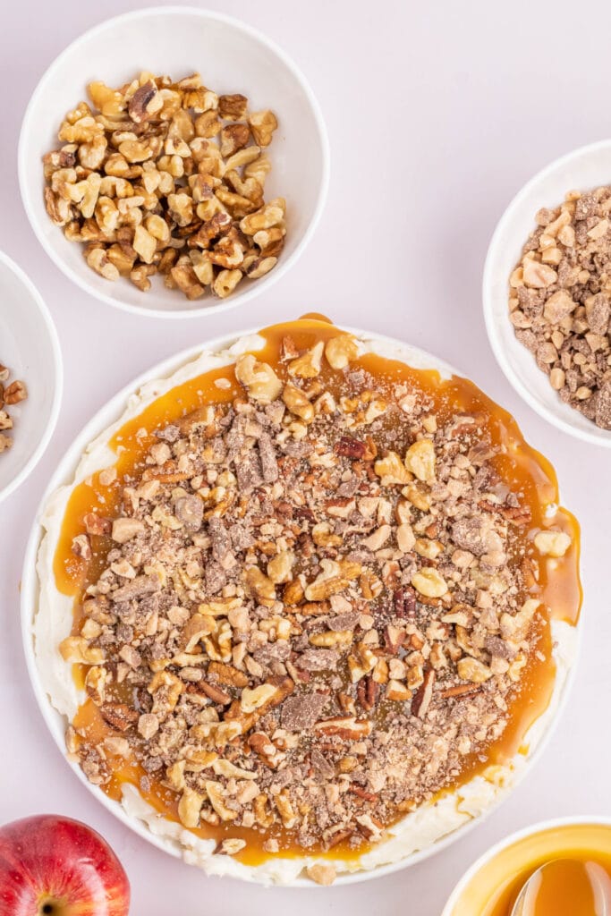 Toffee bits sprinkled over caramel and nut topping for caramel apple dip.
