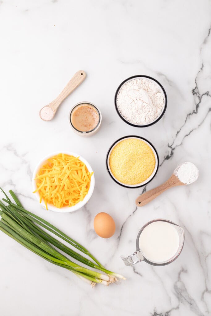 Ingredients for Cheddar Onion Cornbread on a marble surface, including flour, cornmeal, shredded cheese, milk, egg, and green onions.