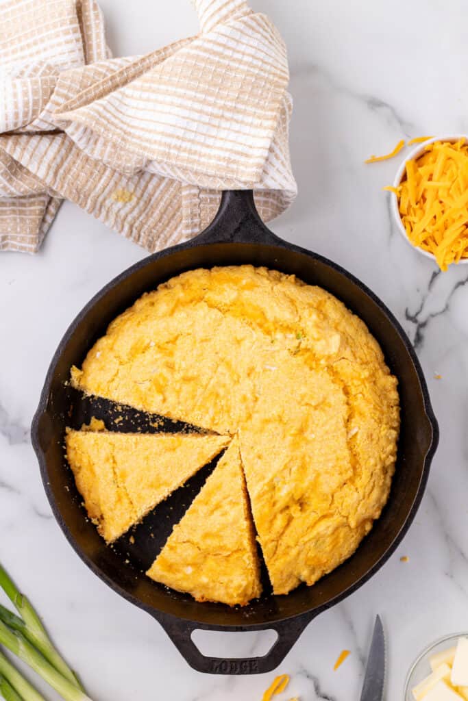 Sliced Cheddar Onion Cornbread in a cast iron skillet showing golden edges and a soft crumb.