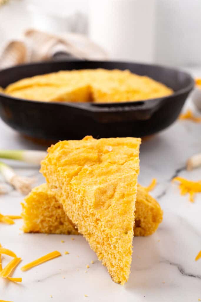 Triangular slices of Cheddar Onion Cornbread stacked on a marble surface with the skillet in the background.