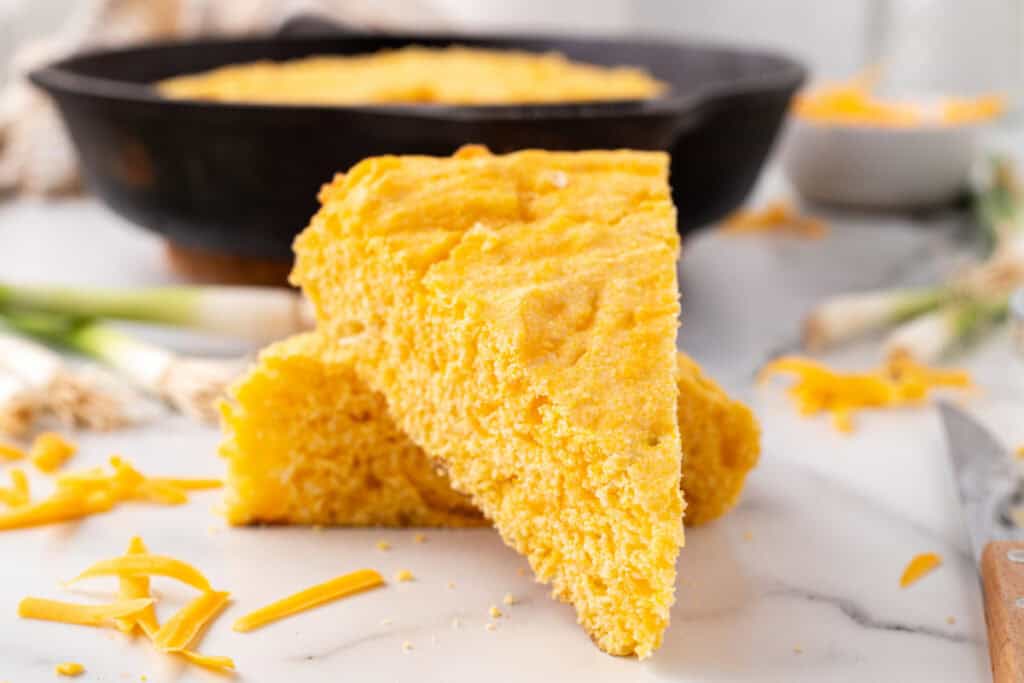 Close-up of two slices of Cheddar Onion Cornbread with visible bits of melted cheese and a golden crumb.