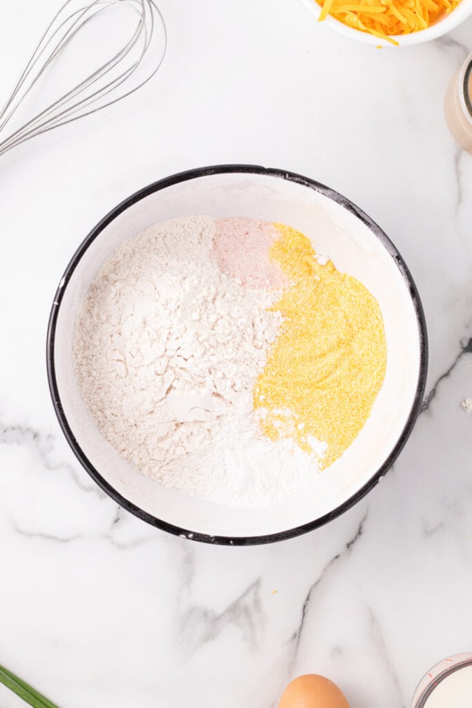 Mixing bowl with flour, cornmeal, salt, and baking powder ready to be whisked together for Cheddar Onion Cornbread batter.