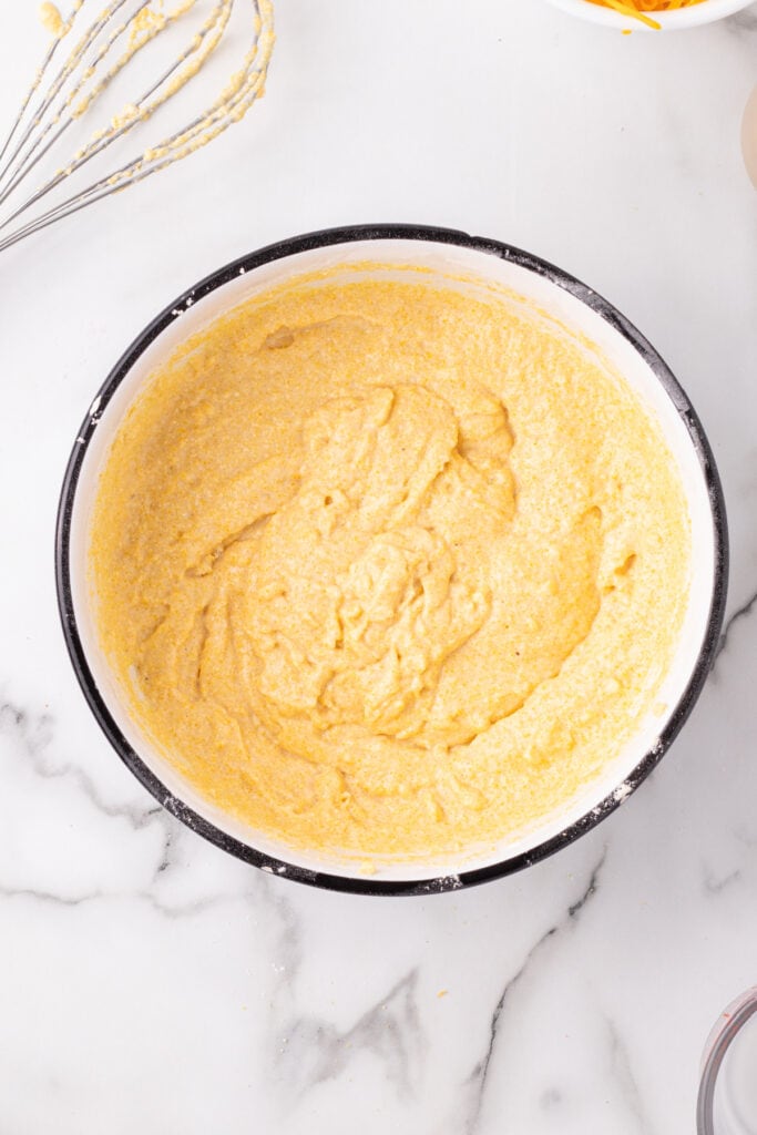 Partially mixed Cheddar Onion Cornbread batter showing a smooth, thick consistency in a white bowl.