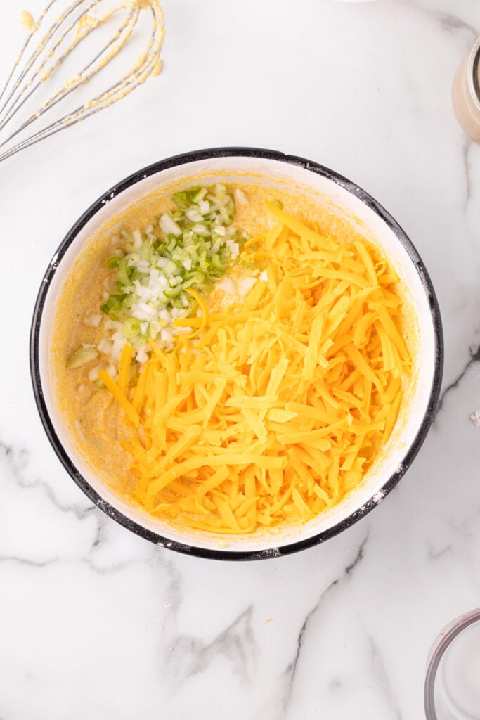 Shredded Cheddar cheese and chopped green onions added to the cornbread batter in a mixing bowl.