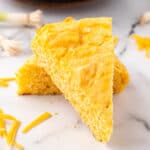 Overhead view of sliced Cheddar Onion Cornbread in a cast iron skillet with a crisp, golden crust.