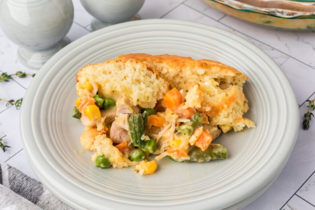 Close-up of a serving of Chicken Biscuit Pot Pie on a white plate showing tender vegetables, chicken, and fluffy biscuit crust.