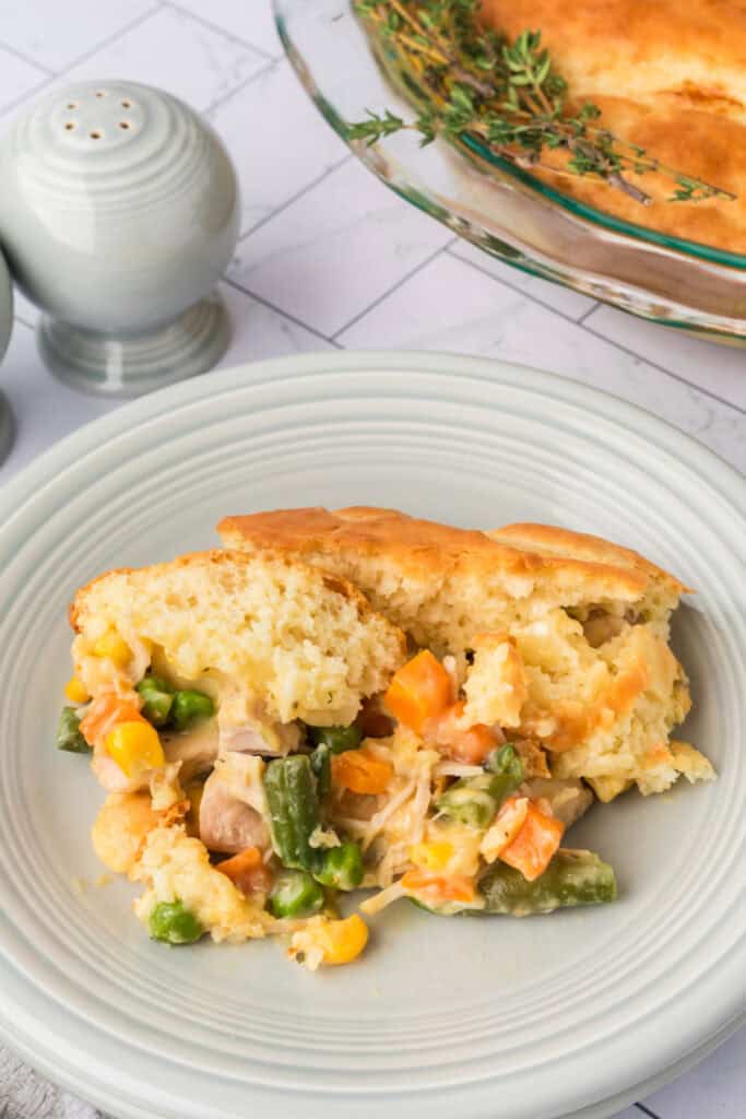 Close-up of a serving of Chicken Biscuit Pot Pie on a white plate showing creamy chicken filling with peas, carrots, and golden biscuit topping.