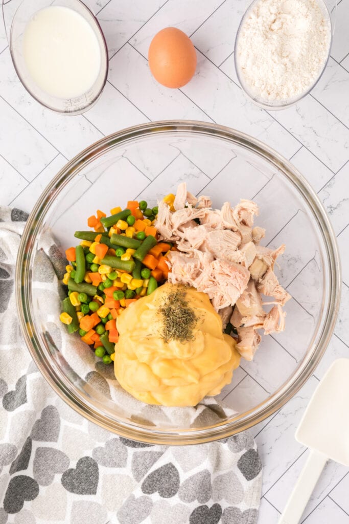 Bowl of chicken, vegetables, and cream of chicken soup being combined with dried thyme for the pot pie filling.