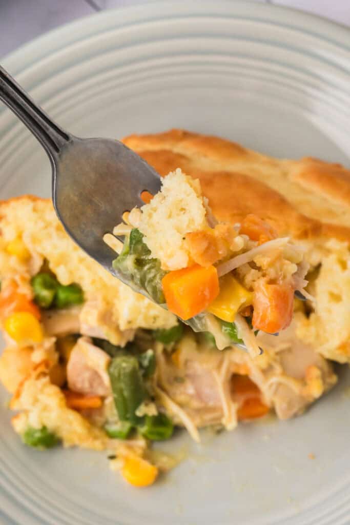 Fork lifting a bite of Chicken Biscuit Pot Pie with biscuit topping, chicken, carrots, peas, and corn in a creamy sauce.