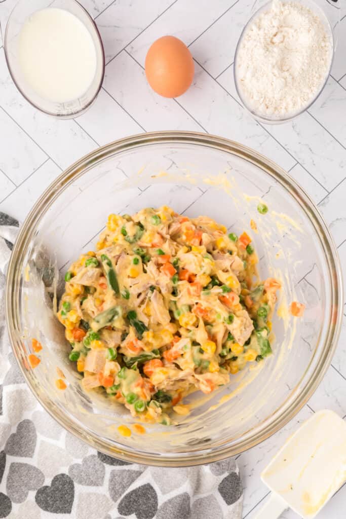Mixed chicken, vegetables, and soup creating a creamy Chicken Biscuit Pot Pie filling in a glass bowl.