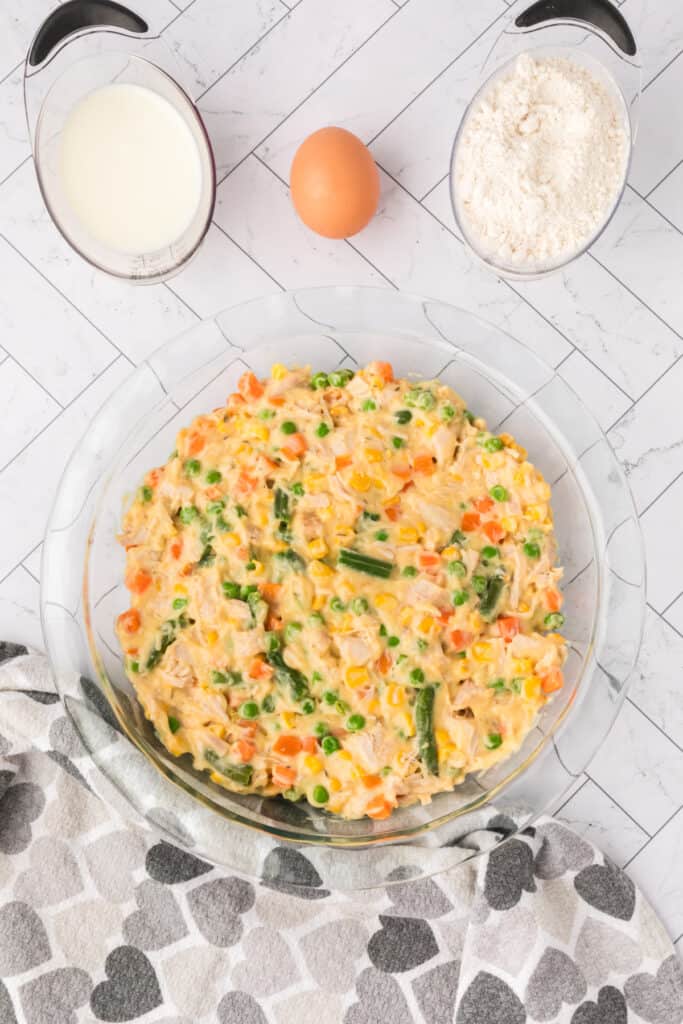 Chicken pot pie filling spread evenly in a clear pie dish before adding biscuit topping.