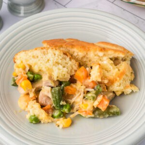 Square crop of Chicken Biscuit Pot Pie on a white plate with colorful vegetables and golden brown biscuit topping, ready to serve.