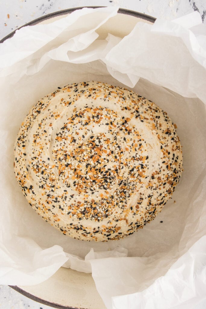 Everything bagel dough placed in a parchment-lined Dutch oven, ready to bake.