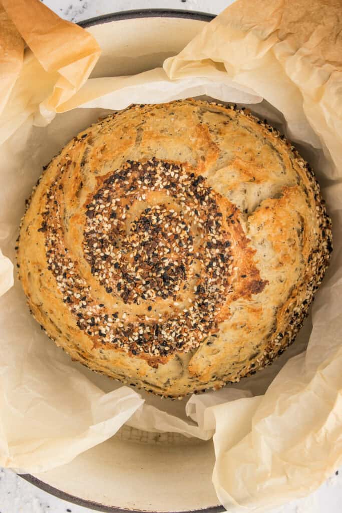 Freshly baked everything bagel bread with a golden crust inside a parchment-lined Dutch oven.