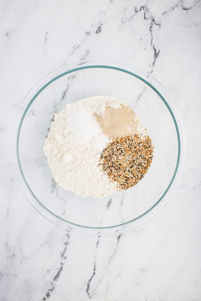 Mixing bowl with flour, salt, yeast, sugar, and everything bagel seasoning before combining.