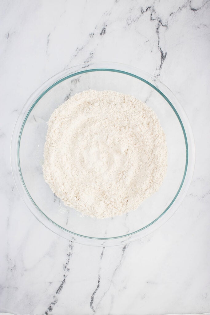 Dry ingredients for everything bagel bread mixed together in a clear glass bowl.