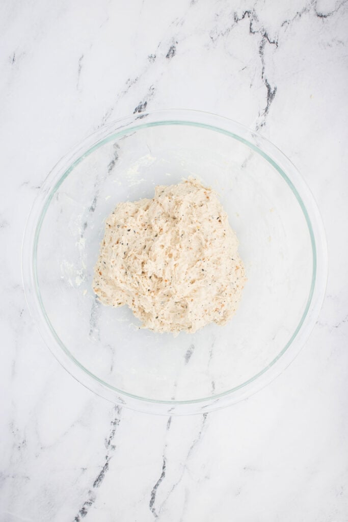 Everything bagel dough mixed into a shaggy, sticky consistency in a large bowl.