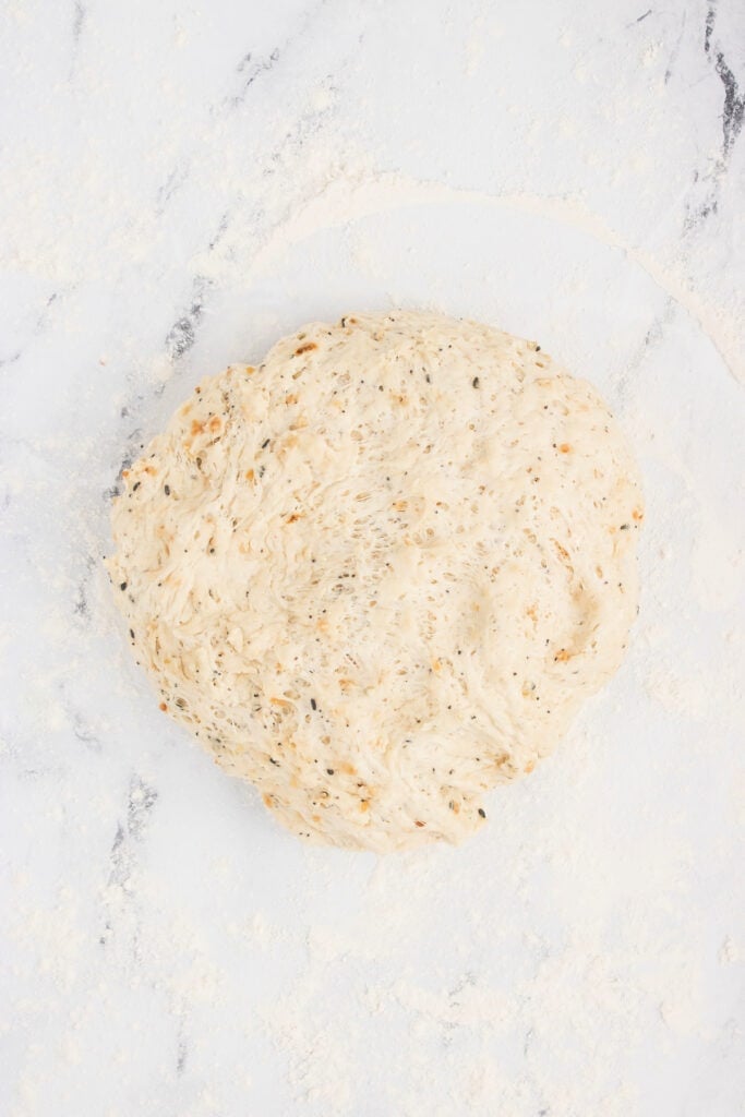 Risen everything bagel dough turned out onto a floured surface, ready to shape.