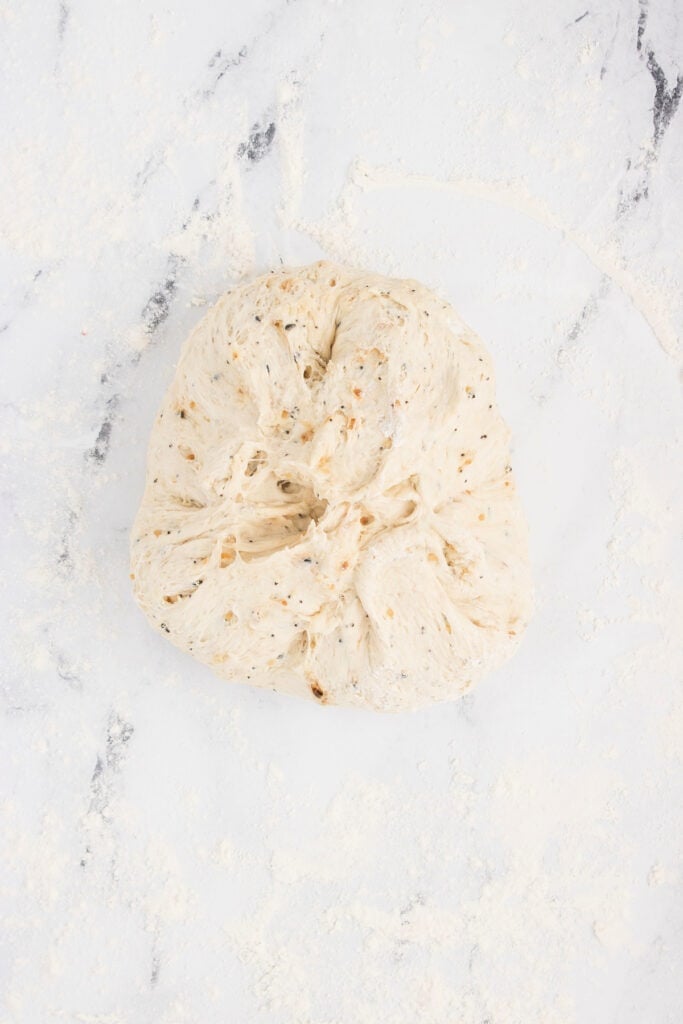 Everything bagel dough folded and tucked to shape into a round loaf.
