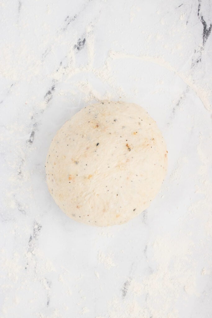 Smooth round loaf of everything bagel dough resting on a floured surface.