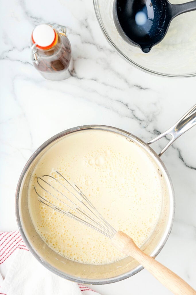 Saucepan with whisk inside, filled with tempered eggnog mixture before thickening.