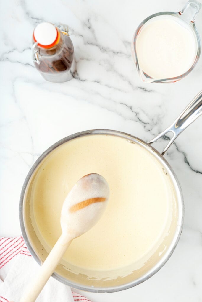 Eggnog mixture in saucepan with wooden spoon showing the line test for coating thickness.