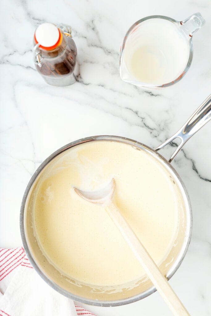 Cooked eggnog in a saucepan with a wooden spoon resting inside, ready for straining.
