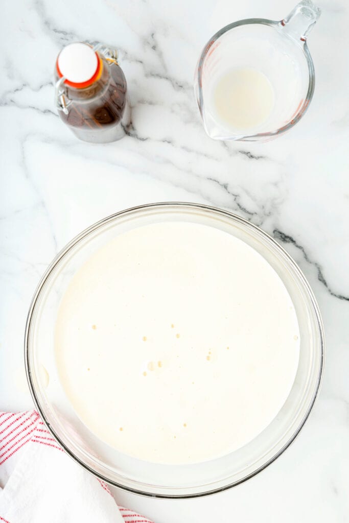 Smooth strained eggnog sitting in a glass mixing bowl on a marble counter.