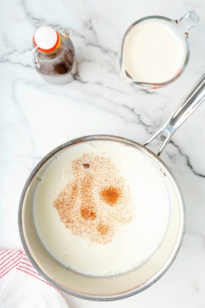 Milk in a saucepan sprinkled with nutmeg and cinnamon before stirring.