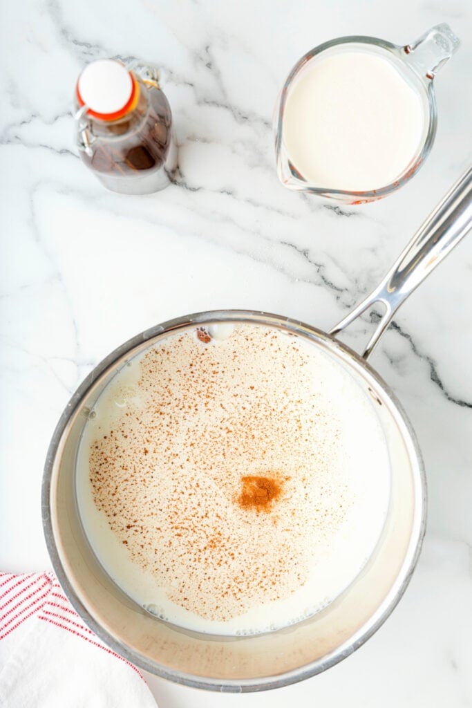 Spiced milk simmering in a saucepan with ground nutmeg and cinnamon on top.