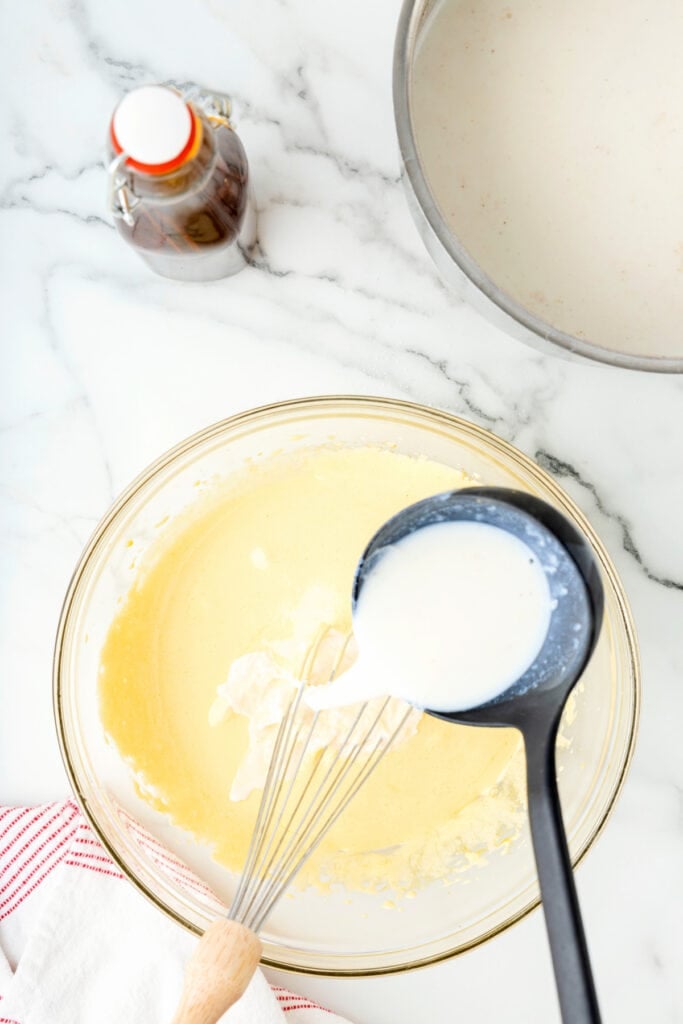 Warm milk mixture being ladled into the egg yolk mixture while whisking.