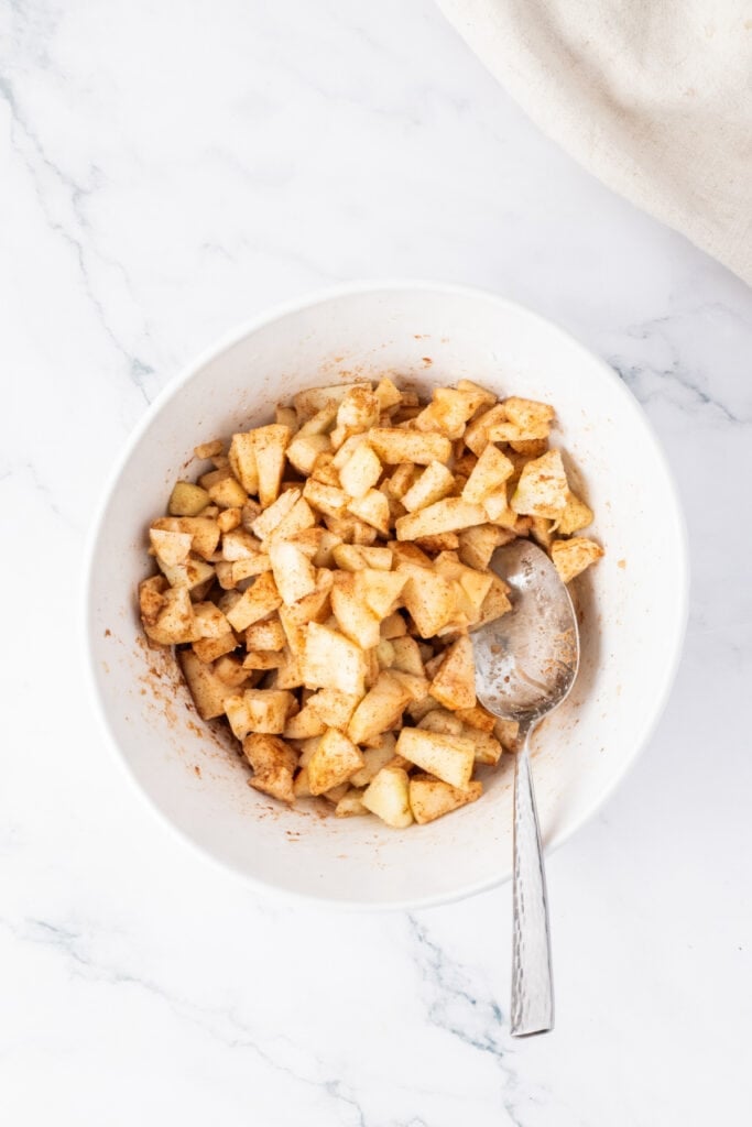 Bowl of diced apples mixed with sugar, cinnamon, and vanilla for the spiced apple topping layer.