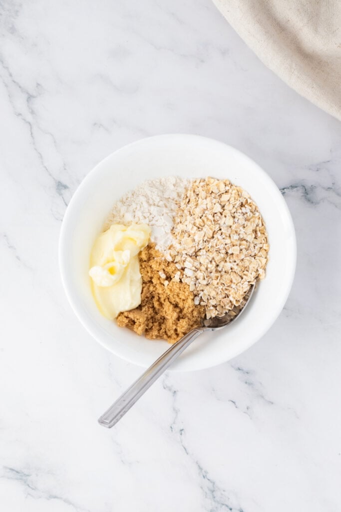 Bowl containing flour, oats, brown sugar, and butter ready to mix for the crumble topping.
