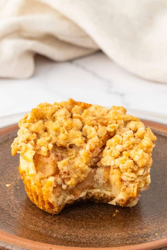 Mini Apple Crumble Cheesecake with a bite taken out, showing layers of cheesecake, apple, and crumble.