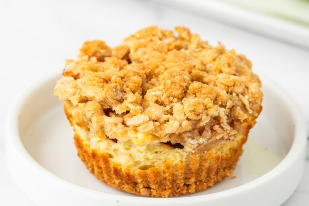 Single Mini Apple Crumble Cheesecake served on a white dish with a crisp oat topping and creamy layer.