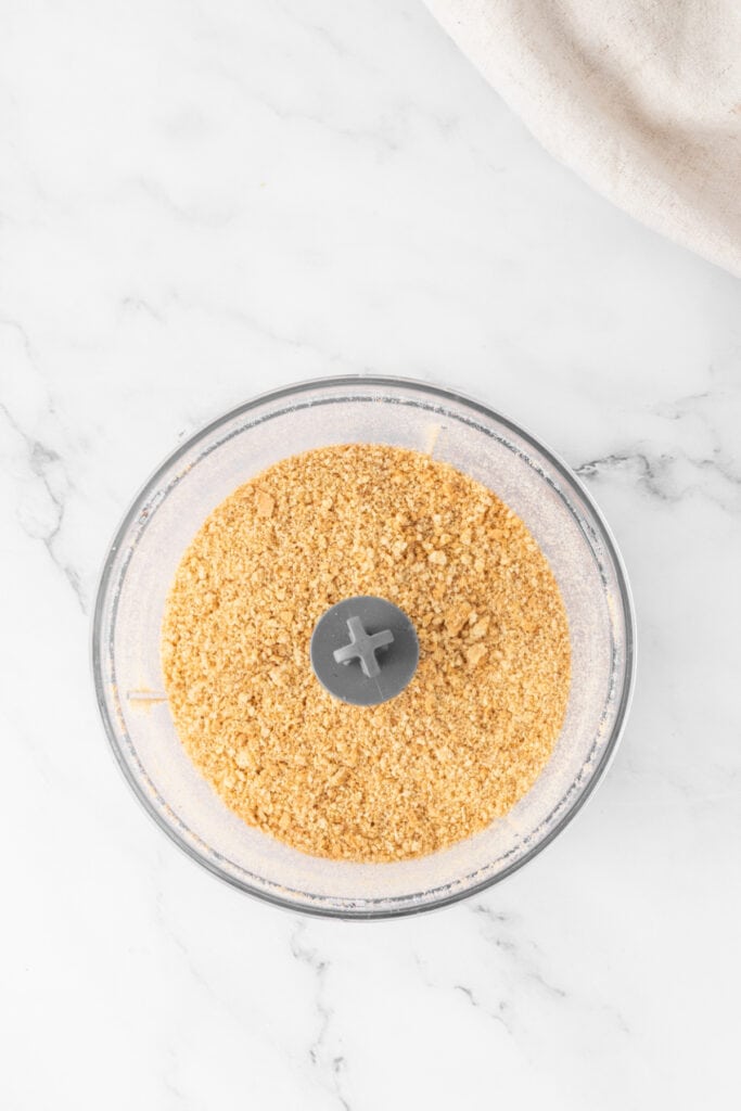 Crushed graham cracker crumbs in a food processor after pulsing, showing a fine, even texture.