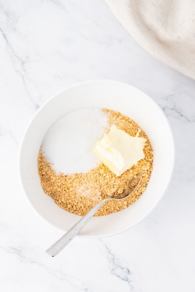 Mixing bowl with graham cracker crumbs, sugar, and melted butter ready to combine for the crust.