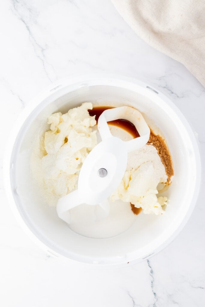 Mixing bowl with cream cheese, sugar, flour, and vanilla in a stand mixer ready to be blended for the cheesecake filling.