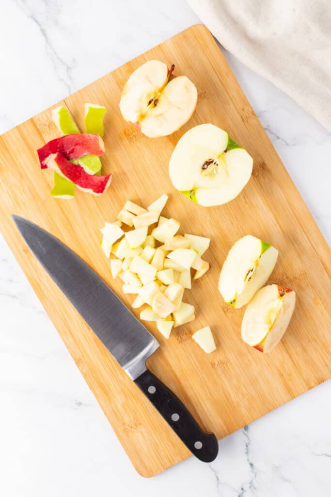 Cutting board with peeled and diced apples and a knife, showing prep for the apple crumble layer.