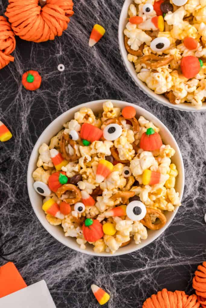 Two bowls of Monster Mash Popcorn with candy eyeballs and pumpkins on a Halloween-themed background.